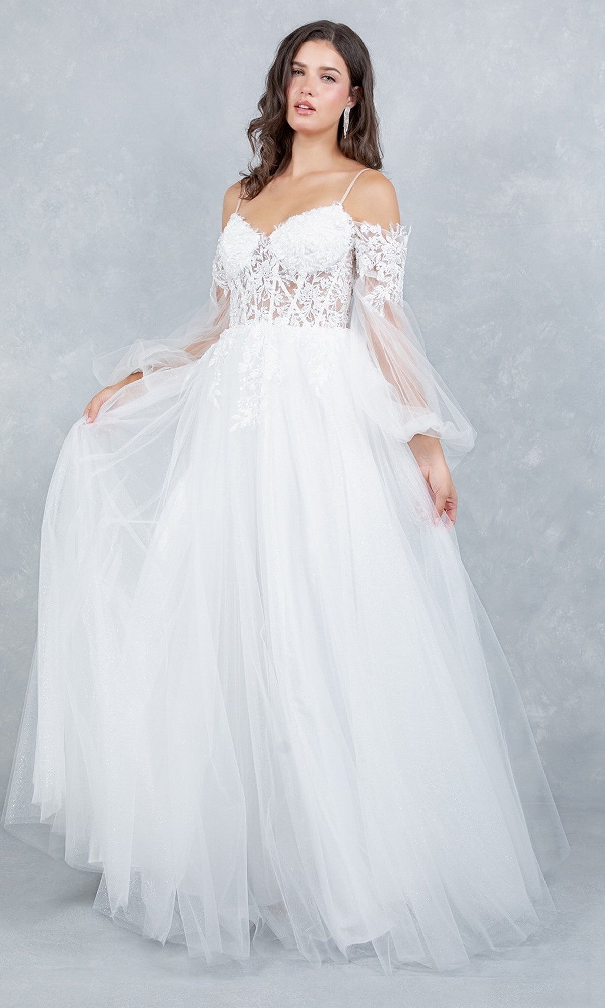 A woman wearing the Cinderella Couture 4234 long formal dress, featuring a lace applique bodice, sheer sleeves, and a flowing tulle skirt, stands against a light gray textured background.